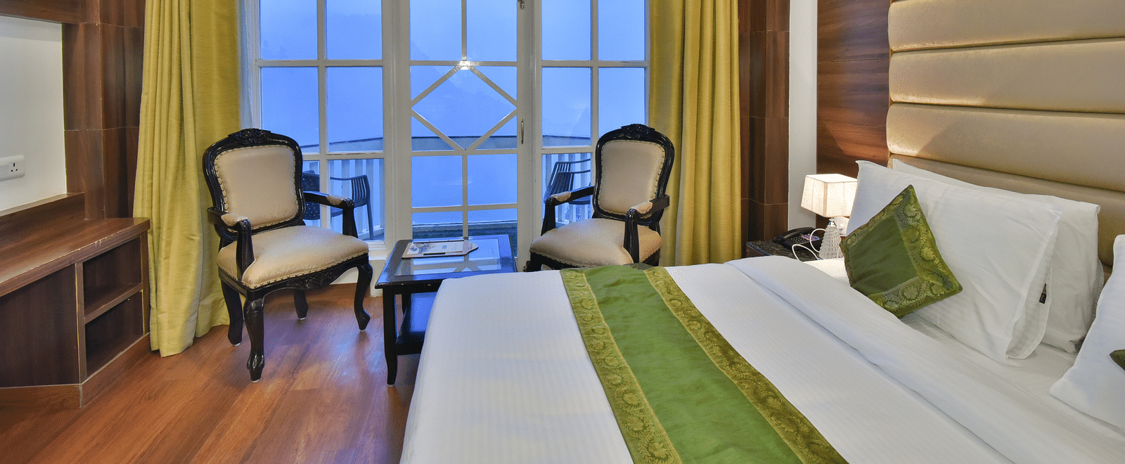 A large bed next to two chairs placed near a large window in the Premium Room at DLS Highland Resort and Spa, Mussoorie.